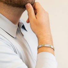 Male model wearing Alluring bracelet showing matte and gold interlocking links, hand resting on chin.