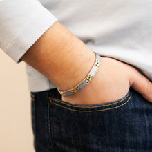 Male model wearing Alluring bracelet with matte stainless steel links and polished gold spacers, hand in pocket.