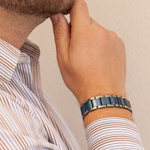 Male model wearing the Blue Moon titanium bracelet with matte blue links and polished edges, hand resting on chin.