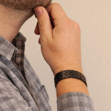 Male model wearing the Brilliant Black matte stainless steel bracelet, hand resting on chin to display engraved matte links and modern masculine style.