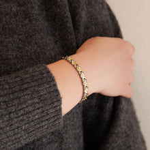 Female model wearing Duet bracelet with intertwined gold and steel links, hand resting on opposite arm.