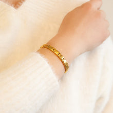 Luminosity gold stainless steel bracelet on wrist catching light, showing elegant matte and polished contrast.
