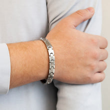 Male model wearing Maverick bracelet with interlocking puzzle links, hand resting on opposite arm.