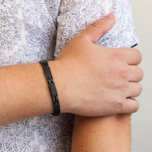 Male model wearing Millennial bracelet with black geometric interlocking links, hand resting on opposite arm.