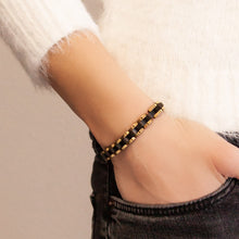 Model wearing the Perfect Balance black and gold stainless steel bracelet with hand in pocket, showing bold two-tone link design.