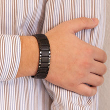 Male model resting hand on opposite arm while wearing Precious Black titanium bracelet, highlighting its geometric link design and triple embedded elements.