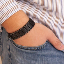 Male model wearing Precious Black titanium bracelet with matte engraved links and polished edges, shown with hand in pocket.