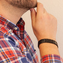 Male model wearing the Pristine Black polished stainless steel bracelet, hand resting on chin to display bold checkered pattern and mirror finish.
