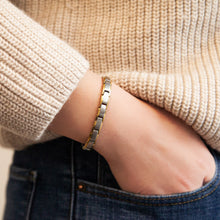 Female model wearing SandStorm bracelet with matte stainless steel links and gold borders, hand in pocket.