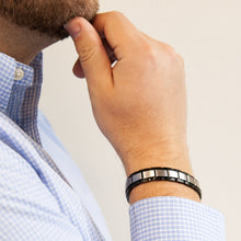 Male model wearing Swell bracelet with angular stainless steel links and polished black borders, hand resting on chin.